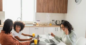 A family using phones, a tablet and a laptop together at a kitchen table.