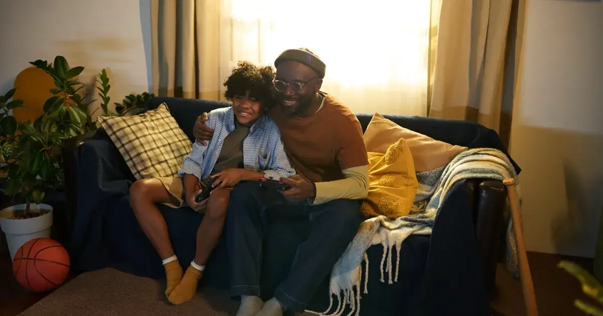 A parent and child playing video games together on a sofa at home.